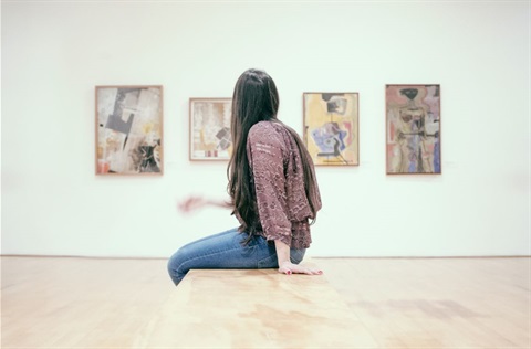 woman sitting in front of an art gallery wall looking at a painting