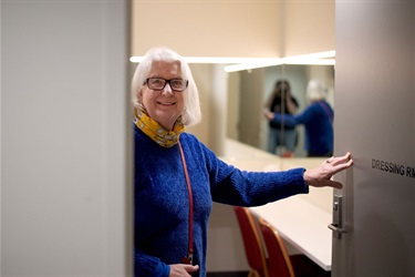 A lady holds open the BMH dressing room door smiling as she looks at the facilities