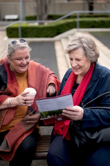 Two women smile in conversation while they are looking at the BMH prospectus document outside the hall