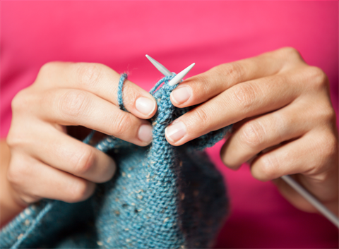 close up image of hands knitting blue wool