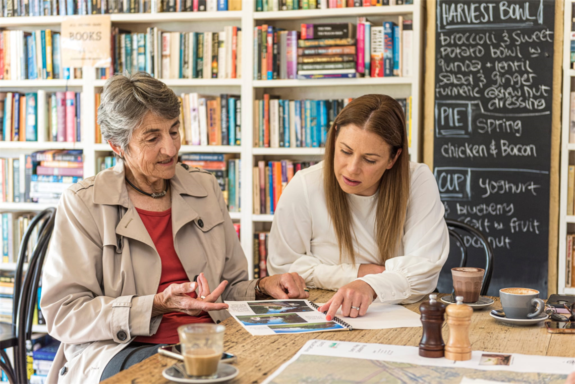 Image of 2 women at a cafe discussing the contents of a report or brochure