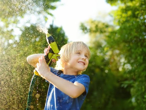 Boy playing with a garden hose spraying water in the air