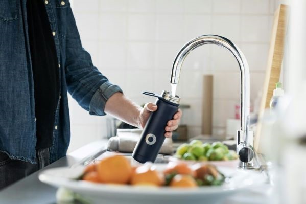 Man filling reusable bottle at a kitchen tap with bowl of fruit in the foreground