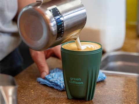Barista pouring a coffee into a green caffeen cup 